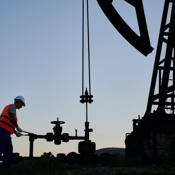 Man wearing a hard hat standing beside an oil well.